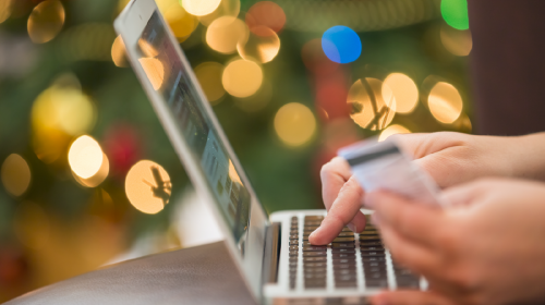 Hand typing on keyboard with credit card in other hand in front of Christmas tree